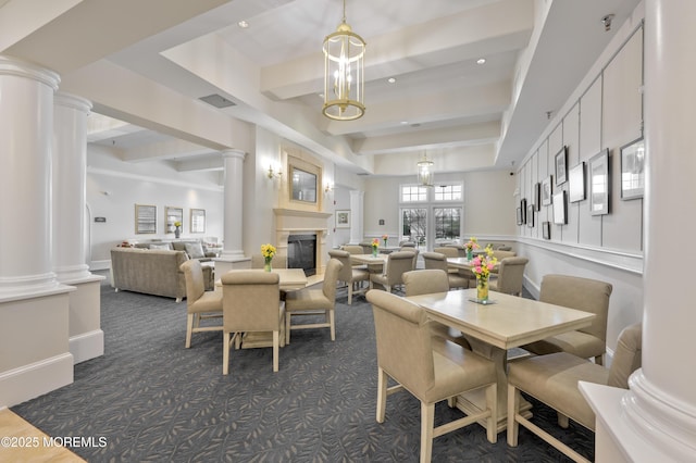 dining space with beamed ceiling, decorative columns, a glass covered fireplace, and dark colored carpet
