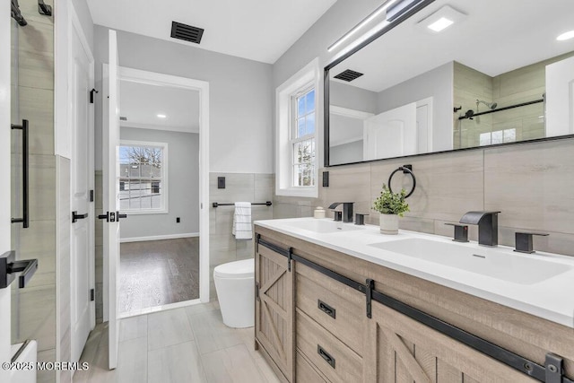 full bath featuring tile walls, a sink, and visible vents