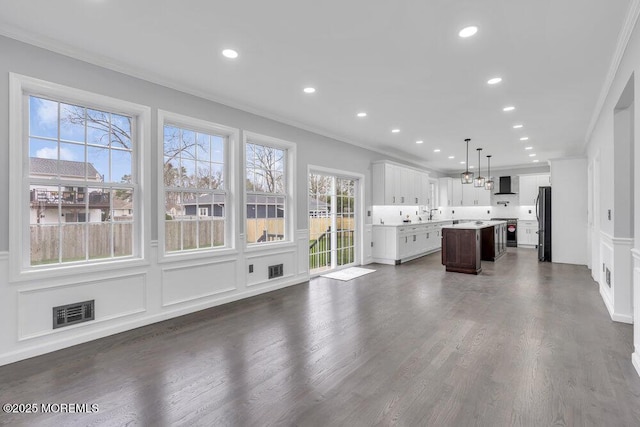 unfurnished living room featuring recessed lighting, visible vents, ornamental molding, and a decorative wall