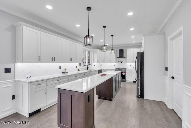 kitchen with appliances with stainless steel finishes, a center island, wood finished floors, ornamental molding, and wall chimney exhaust hood