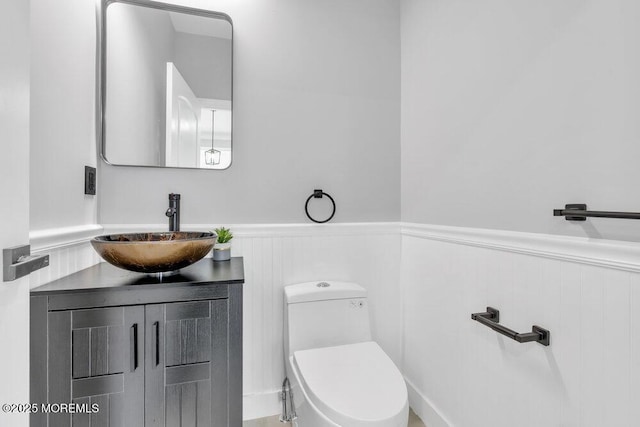 half bath featuring vanity, toilet, and a wainscoted wall
