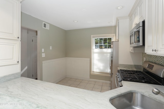 kitchen featuring light stone countertops, stainless steel appliances, white cabinetry, light tile patterned floors, and visible vents