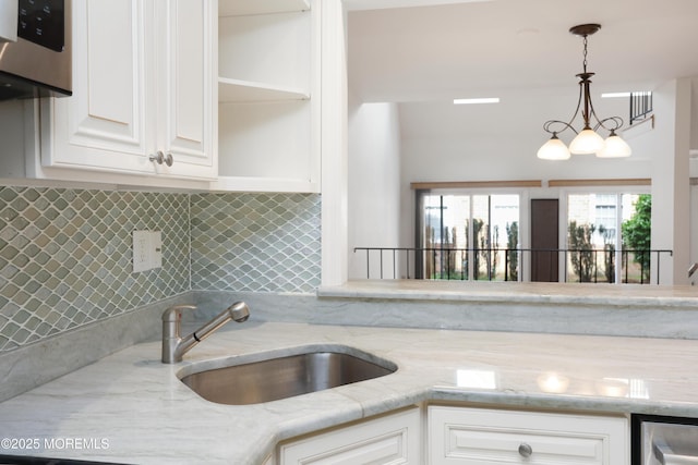 kitchen featuring white cabinets, light stone counters, a sink, decorative light fixtures, and backsplash