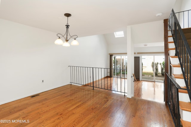 spare room featuring visible vents, stairway, baseboards, wood-type flooring, and a notable chandelier