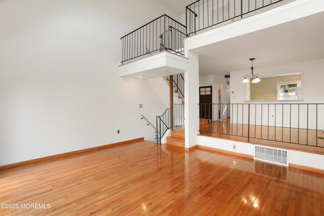 unfurnished living room featuring visible vents, baseboards, an inviting chandelier, a high ceiling, and hardwood / wood-style floors