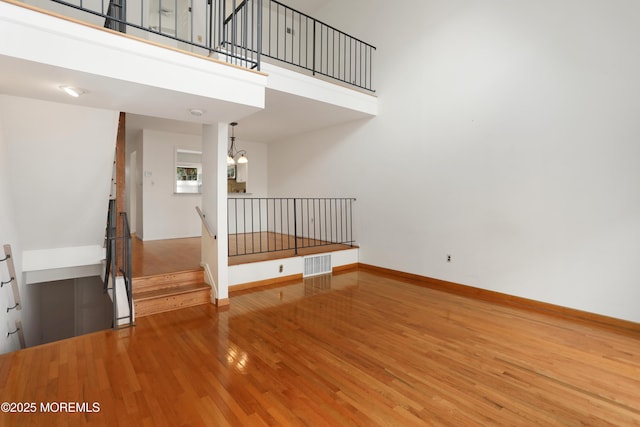 interior space with an inviting chandelier, baseboards, wood finished floors, a towering ceiling, and visible vents