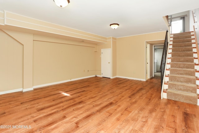 unfurnished living room featuring baseboards, light wood-style flooring, crown molding, and stairway