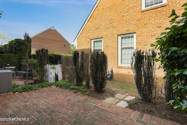 view of home's exterior with a patio, central AC, brick siding, and fence