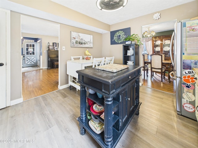 kitchen featuring freestanding refrigerator, a chandelier, light wood-style floors, dark cabinets, and baseboards