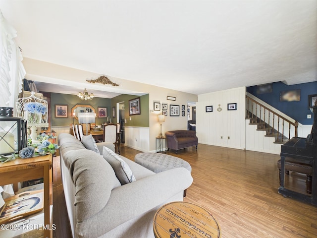 living area with stairs, wood finished floors, a wainscoted wall, and a chandelier