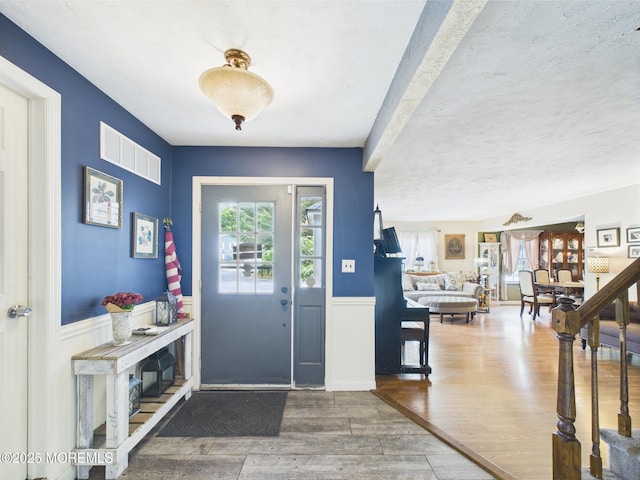 entrance foyer with wood finished floors and a wainscoted wall
