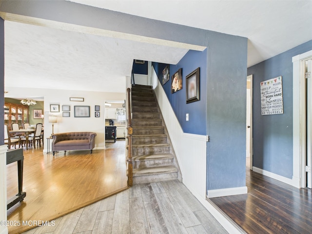 stairway featuring a chandelier, wood finished floors, and wainscoting