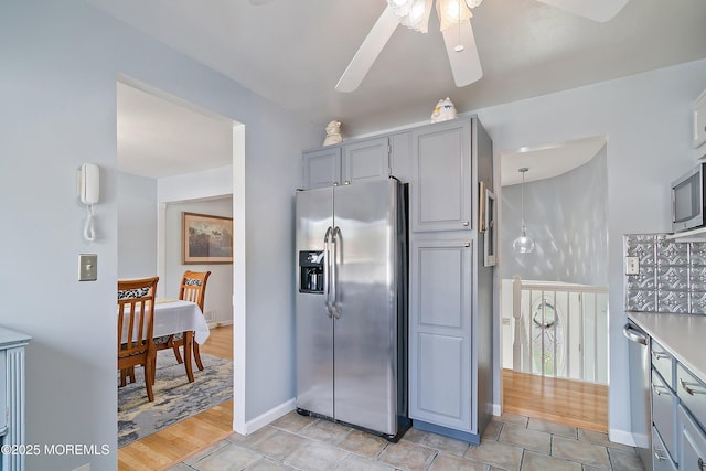 kitchen featuring appliances with stainless steel finishes, gray cabinetry, a ceiling fan, baseboards, and light countertops