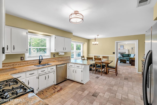 kitchen featuring stainless steel appliances, a sink, white cabinetry, a peninsula, and light stone finish floors
