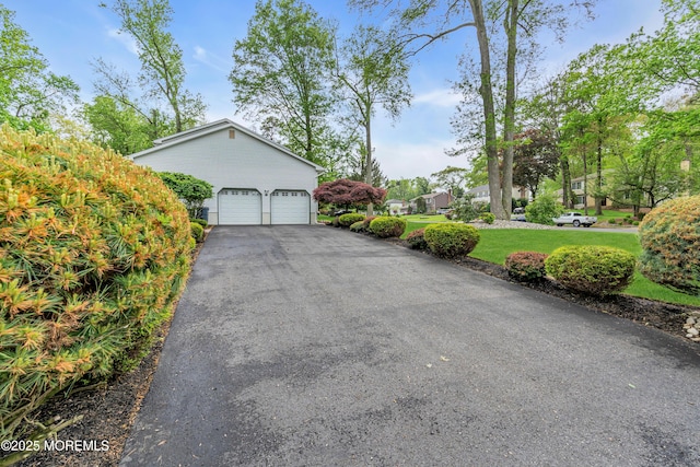 view of property exterior with asphalt driveway, an attached garage, and a yard