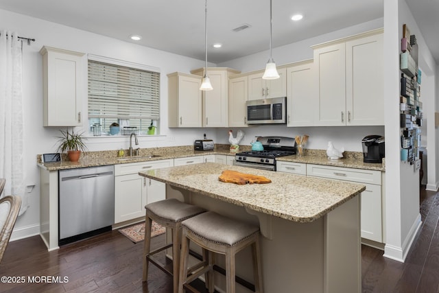 kitchen with stainless steel appliances, a sink, a kitchen island, a kitchen breakfast bar, and dark wood finished floors