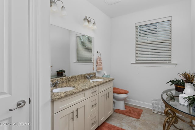 bathroom featuring baseboards, double vanity, and toilet