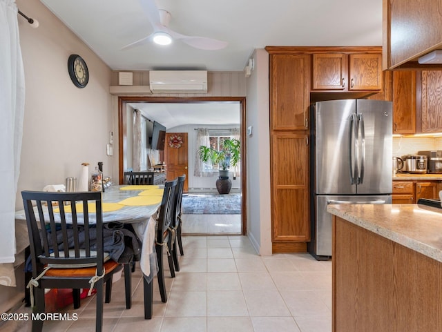 kitchen with freestanding refrigerator, a wall mounted AC, brown cabinets, ceiling fan, and tasteful backsplash