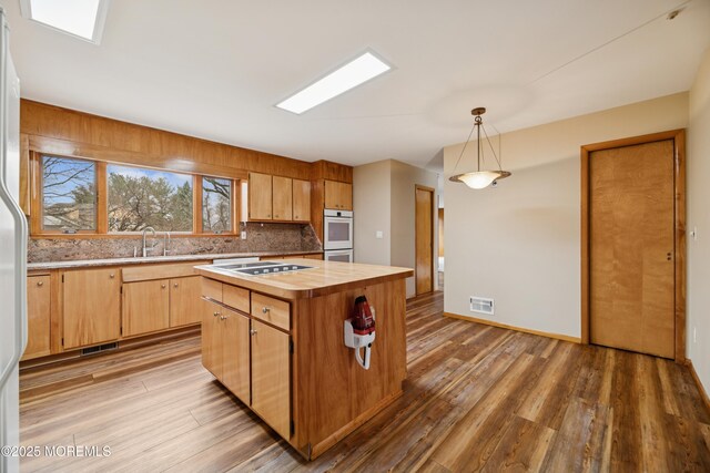 kitchen with butcher block countertops, light wood-style flooring, a kitchen island, a sink, and decorative light fixtures