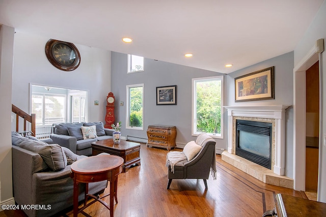 living room featuring a tiled fireplace, a baseboard radiator, wood finished floors, and lofted ceiling