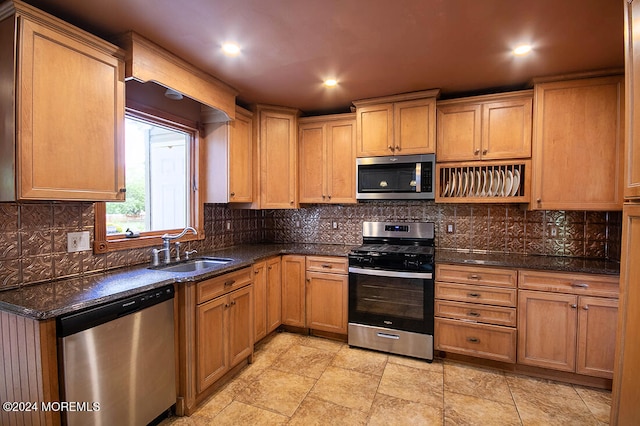 kitchen featuring dark stone counters, stainless steel appliances, a sink, and tasteful backsplash