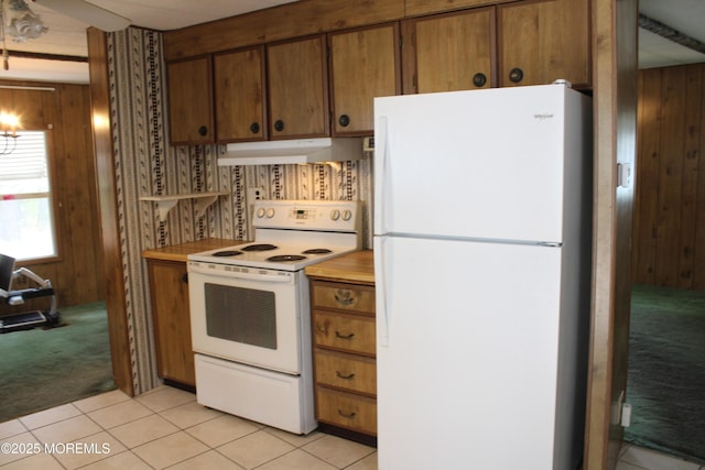kitchen with light colored carpet, wood walls, light countertops, under cabinet range hood, and white appliances