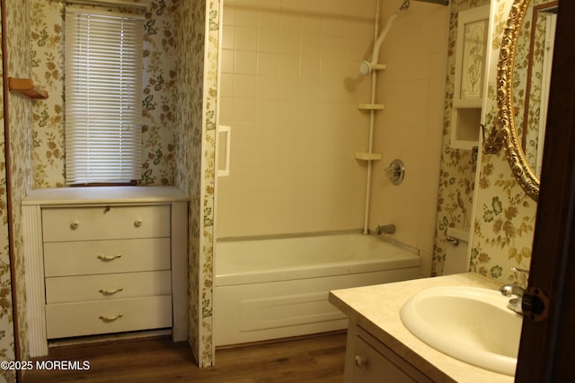 bathroom with wallpapered walls,  shower combination, wood finished floors, and vanity