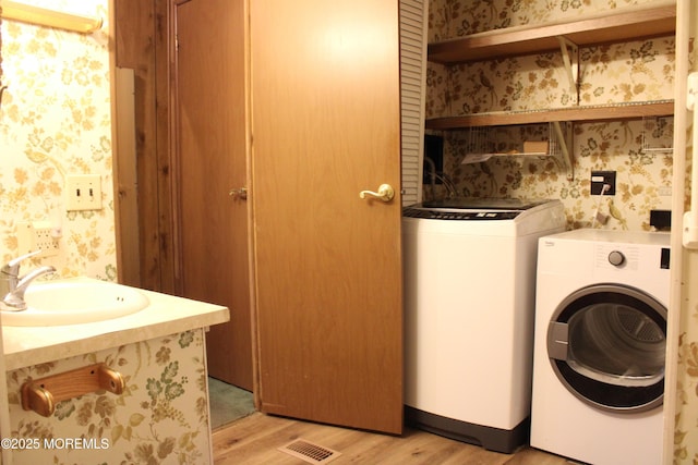 laundry room with light wood-type flooring, a sink, wallpapered walls, and washing machine and clothes dryer