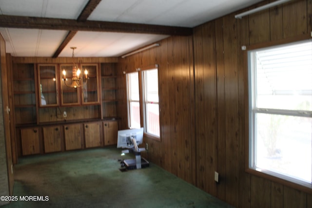 unfurnished dining area featuring wooden walls, carpet floors, beamed ceiling, and a notable chandelier