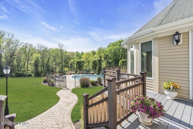 view of swimming pool with a forest view, a lawn, a wooden deck, fence, and a fenced in pool