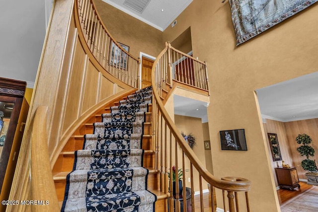 stairway featuring visible vents, a towering ceiling, wood finished floors, baseboards, and ornamental molding