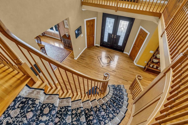 foyer entrance featuring french doors, wood finished floors, stairway, baseboards, and a high ceiling