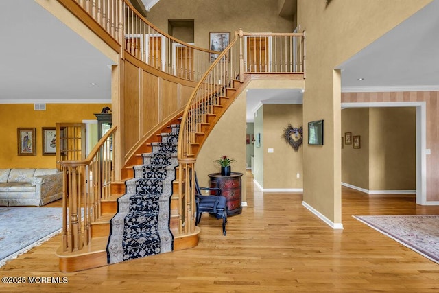 stairway with crown molding, visible vents, a towering ceiling, wood finished floors, and baseboards
