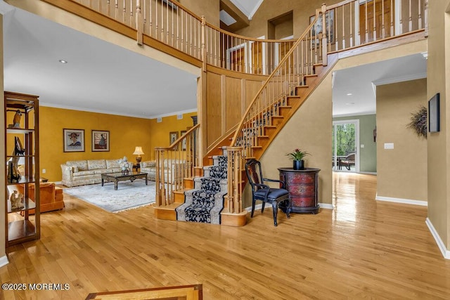 stairs featuring baseboards, ornamental molding, wood finished floors, and a high ceiling