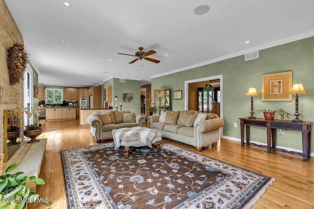living area with crown molding, ceiling fan, visible vents, and light wood-type flooring