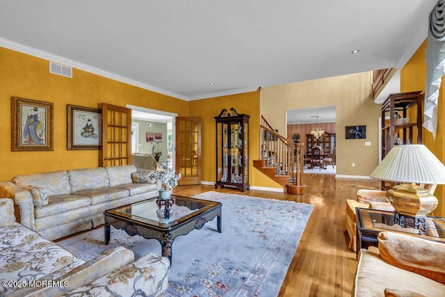 living room with visible vents, baseboards, wood-type flooring, an inviting chandelier, and stairs