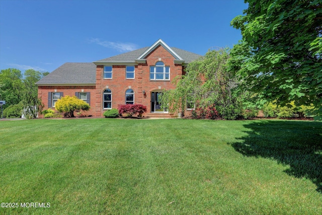 view of front of home with a front lawn, brick siding, and a shingled roof