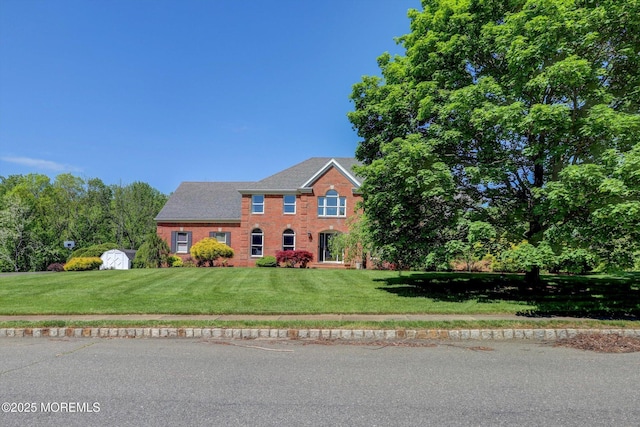 colonial house with a front lawn, a storage unit, brick siding, and an outdoor structure
