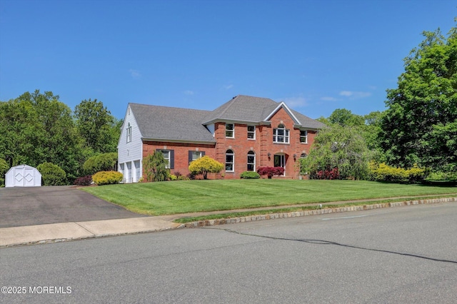 colonial-style house featuring a garage, a front yard, brick siding, and asphalt driveway