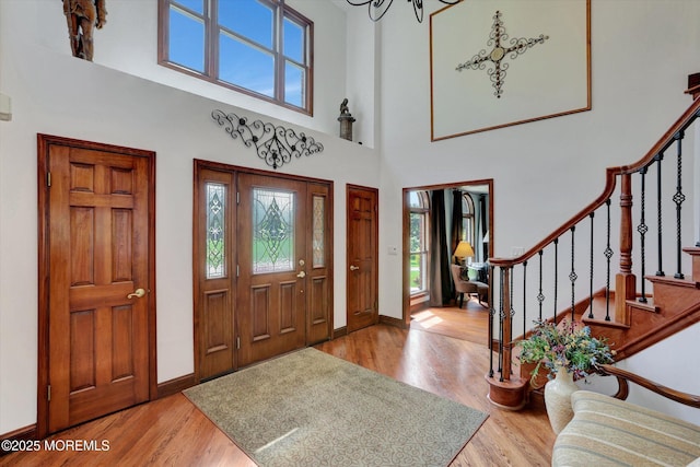 entrance foyer featuring wood finished floors, a high ceiling, baseboards, stairs, and a chandelier