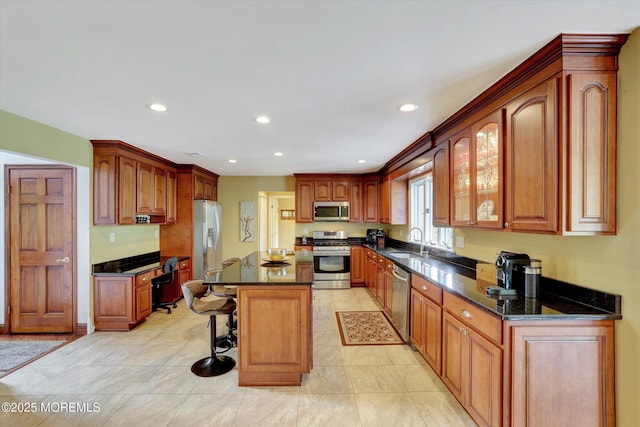 kitchen featuring stainless steel appliances, a sink, a breakfast bar, recessed lighting, and dark stone countertops