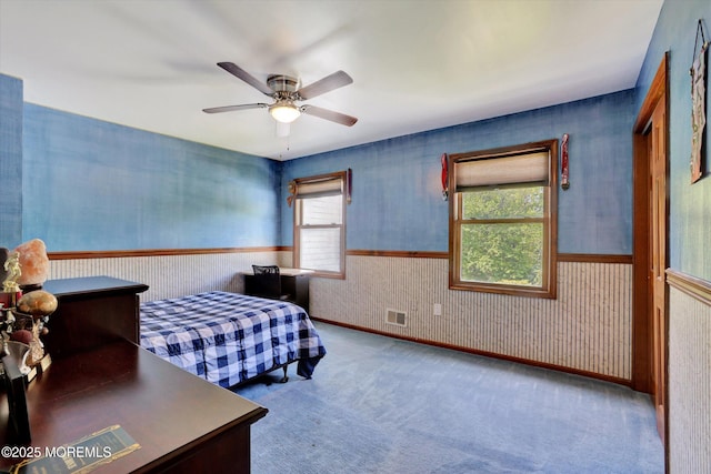 carpeted bedroom featuring wallpapered walls, a wainscoted wall, and a ceiling fan