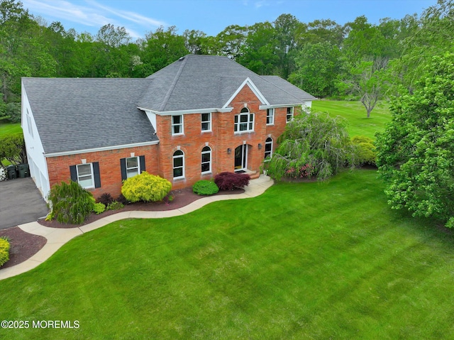 view of front of property featuring roof with shingles, a front lawn, and brick siding
