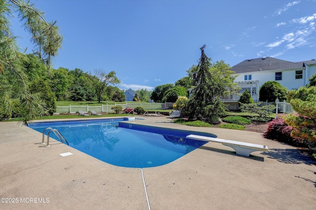 view of swimming pool featuring fence, a diving board, and a patio