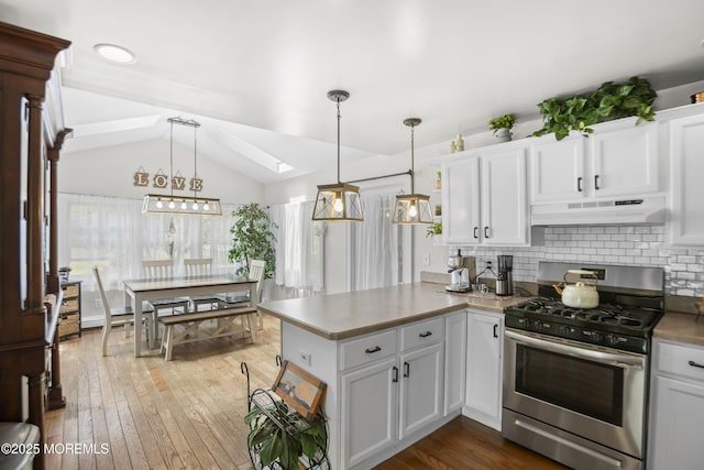 kitchen featuring decorative backsplash, a peninsula, under cabinet range hood, vaulted ceiling with skylight, and stainless steel range with gas stovetop