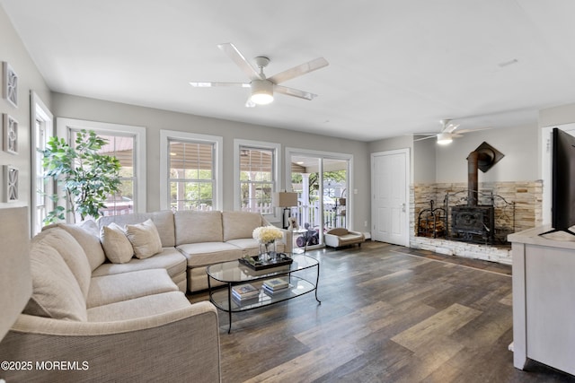 living room featuring a wood stove, a ceiling fan, and dark wood-type flooring