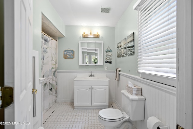 bathroom featuring toilet, visible vents, a wealth of natural light, and a wainscoted wall