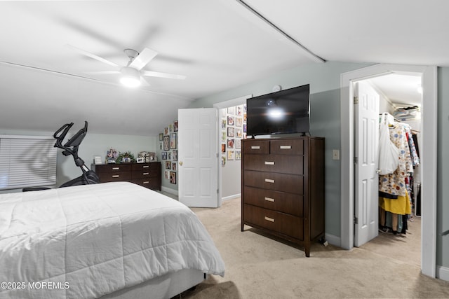 bedroom with lofted ceiling, baseboards, light colored carpet, and a walk in closet