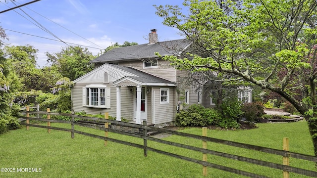 view of front of property with a front lawn, a shingled roof, a chimney, and fence