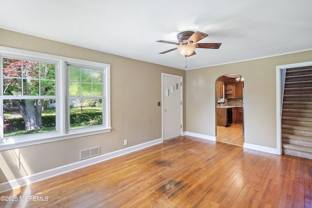 unfurnished room with arched walkways, a ceiling fan, light wood-style floors, baseboards, and stairs